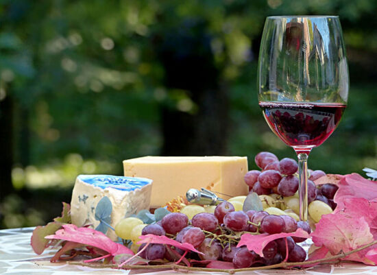 Wein und Käse, angerichtet mit roten und hellen Trauben und herbstlichen Blättern im Freien