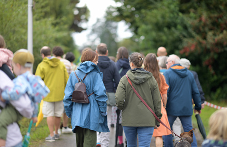 Besucher*innen des Hoffests schlendern gemeinsam einen Weg entlang – viele in Regenjacken, mit entspannter Stimmung.