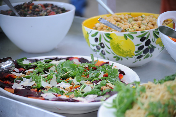 Eine Nahaufnahme von mehreren Schüsseln mit frischen Salaten, die auf einem Tisch angerichtet sind. Einer der Salate enthält Rucola und Käse.