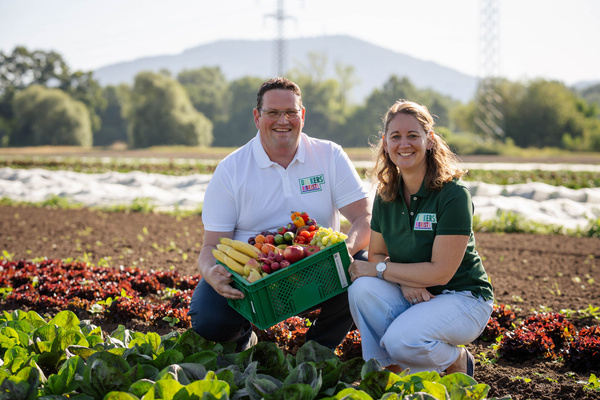 Christoph Decker und Leonie Schittenhelm hocken auf einem Feld in Weitenung und halten eine Ökokiste