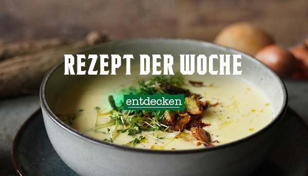 Nahaufnahme einer cremigen Suppe, garniert mit Kräutern und Pilzen, in einer Schüssel. Im Hintergrund liegen Zwiebeln. Text im Bild: „Rezept der Woche – entdecken