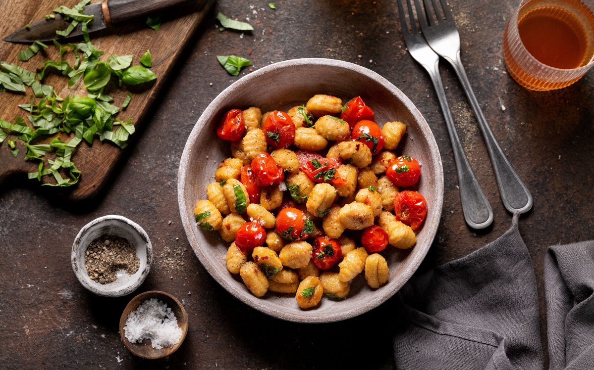 Teller mit frisch zubereiteten Gnocchi, dazu Kräuter und Olivenöl auf einem Tisch.