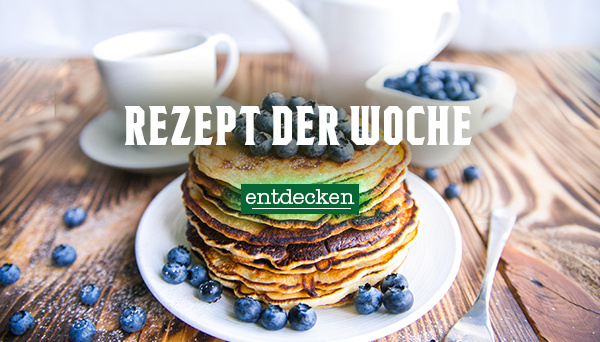 Nahaufnahme einer cremigen Suppe, garniert mit Kräutern und Pilzen, in einer Schüssel. Im Hintergrund liegen Zwiebeln. Text im Bild: „Rezept der Woche – entdecken
