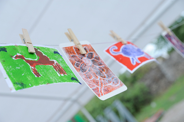 Eine Nahaufnahme von mehreren Kinderzeichnungen, die mit Wäscheklammern an einer Leine aufgehängt sind. Die Zeichnungen zeigen bunte Tiere oder Figuren.